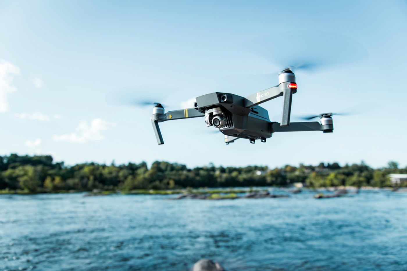 Drone in flight over water near a tree-lined shoreline